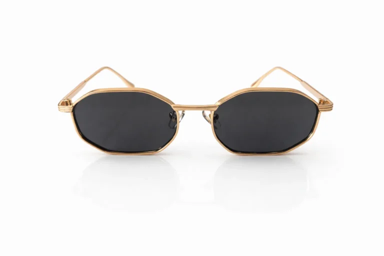 Paire de lunettes de soleil à monture dorée et verres noirs de forme octogonale, sur fond blanc.