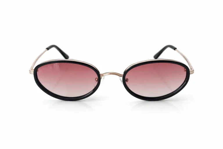 Lunettes de soleil ovales avec monture noire et branches fines dorées, verres dégradé rose pâle sur fond blanc.