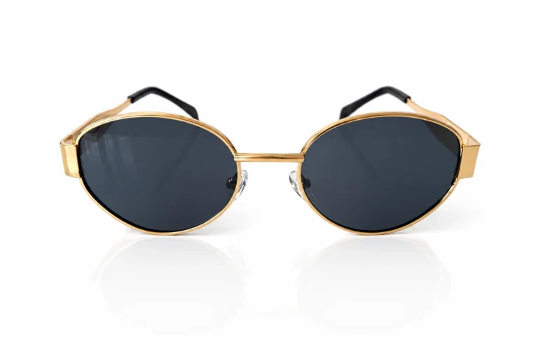 Gros plan sur des lunettes de soleil stylées à monture dorée et verres teintés foncés, posées sur fond blanc.