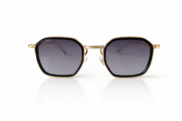 Lunettes de soleil à monture dorée et verres dégradés gris, avec une forme octogonale et un contour noir.
