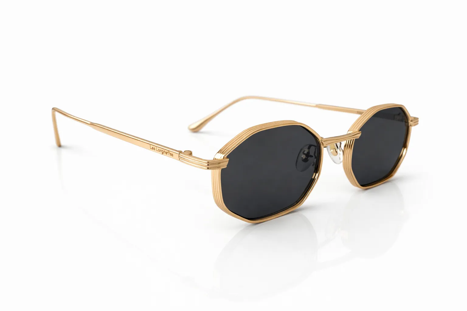 lunettes-soleil-or-hexagonales-verres-noirs Une paire de lunettes de soleil dorées avec une monture hexagonale aux verres fumés noirs, sur fond blanc.